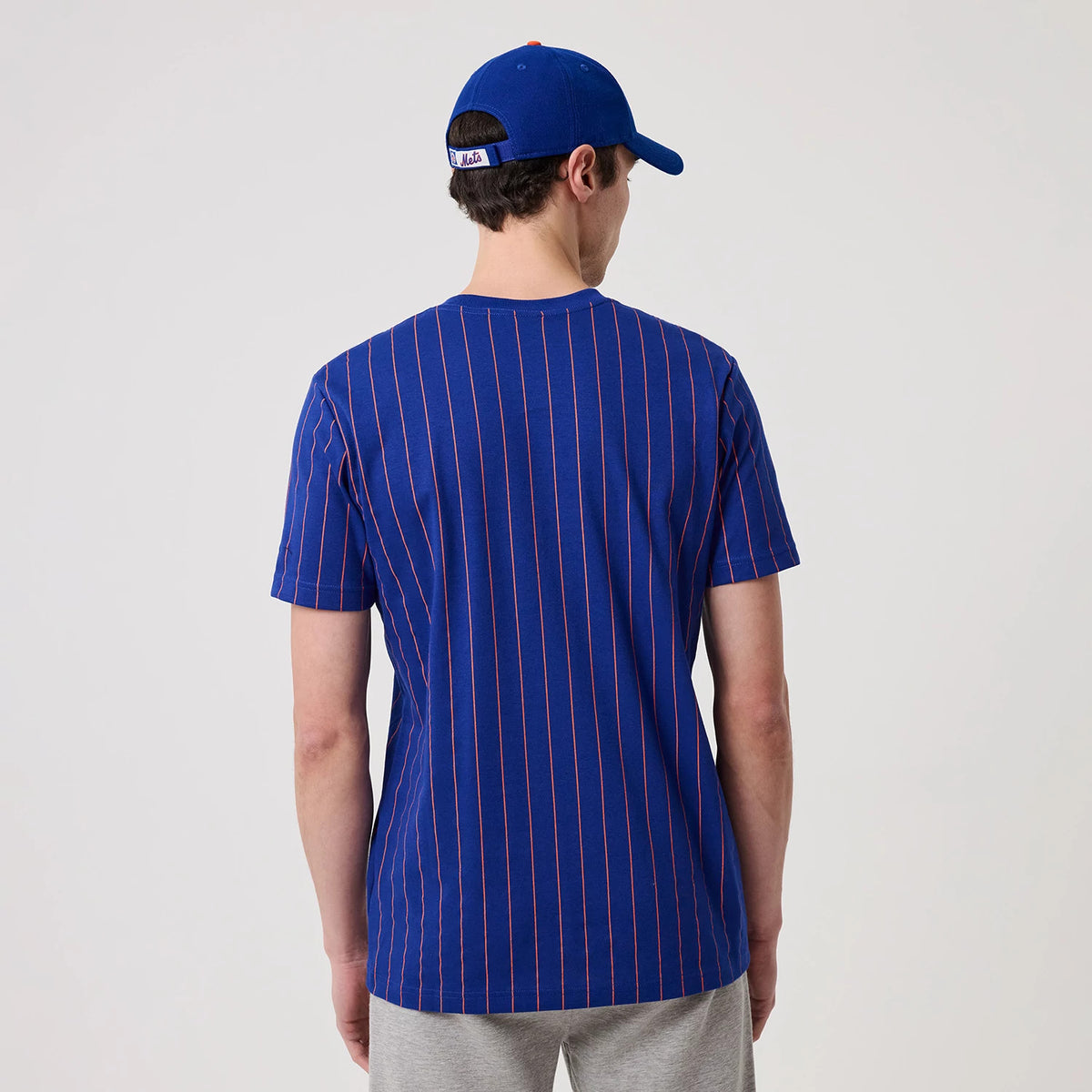 New Era New York Mets MLB Pinstripe Blue T-Shirt, back view on a model showing vertical red pinstripes across the blue fabric and a blue cap, creating a coordinated athletic appearance.