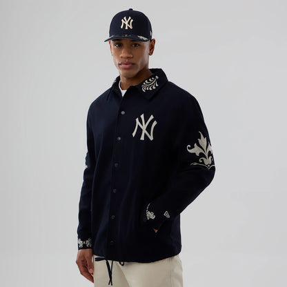 New Era New York Yankees MLB Script Navy Coach Jacket, front view on a model with a matching cap, showing an embroidered NY logo on the left chest, ornate designs on the collar and sleeves, and a small embroidered New Era logo on the wrist.