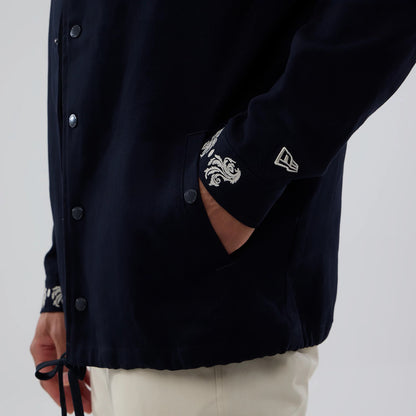 New Era New York Yankees MLB Script Navy Coach Jacket, front three-quarter view showing embroidered patterns on the cuff, white New Era logo on the sleeve, buttoned front closure, and a drawstring at the hem, worn with light trousers.