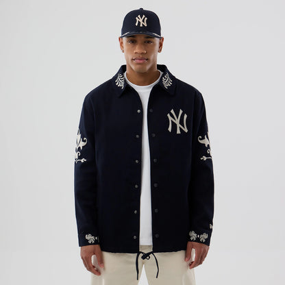 New Era New York Yankees MLB Script Navy Coach Jacket, front view on a model with a matching cap, featuring embroidered NY logo on the left chest, intricate white designs on the sleeves and cuffs, and detailed embroidery on the collar.