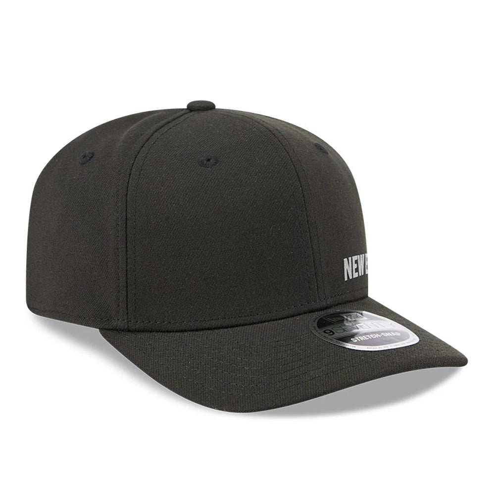 New Era Flawless Black 9SEVENTY Stretch Snap Adjustable Cap, three-quarter view showing the grey embroidered text on the front panel, a slightly curved black visor, and a 9SEVENTY size sticker on the top of the visor.