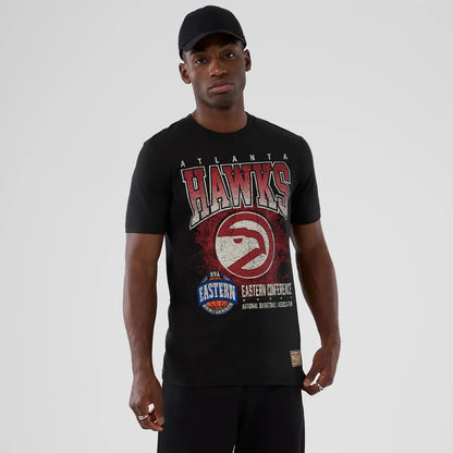 New Era Atlanta Hawks NBA Hardwood Classic Black T-Shirt, front view on-model showing large distressed Hawks logo and lettering across the chest, with additional NBA Eastern Conference graphics and a small woven label at the hem.