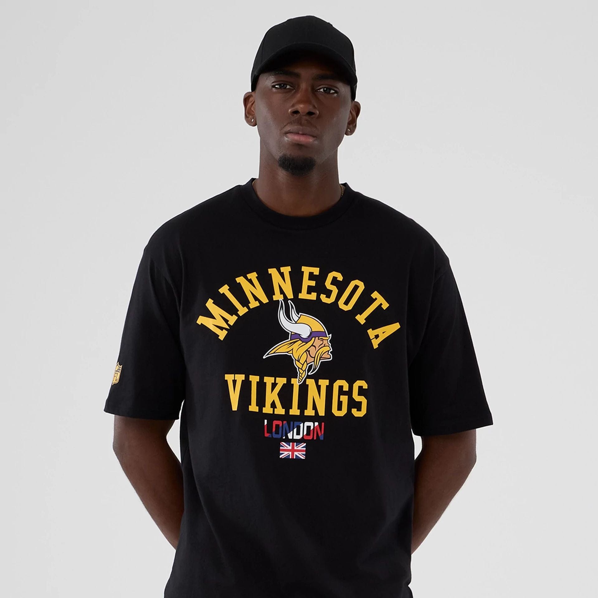 The Male model is wearing Minnesota Vikings NFL International Series Games 2025 Black Oversized T-Shirt  7