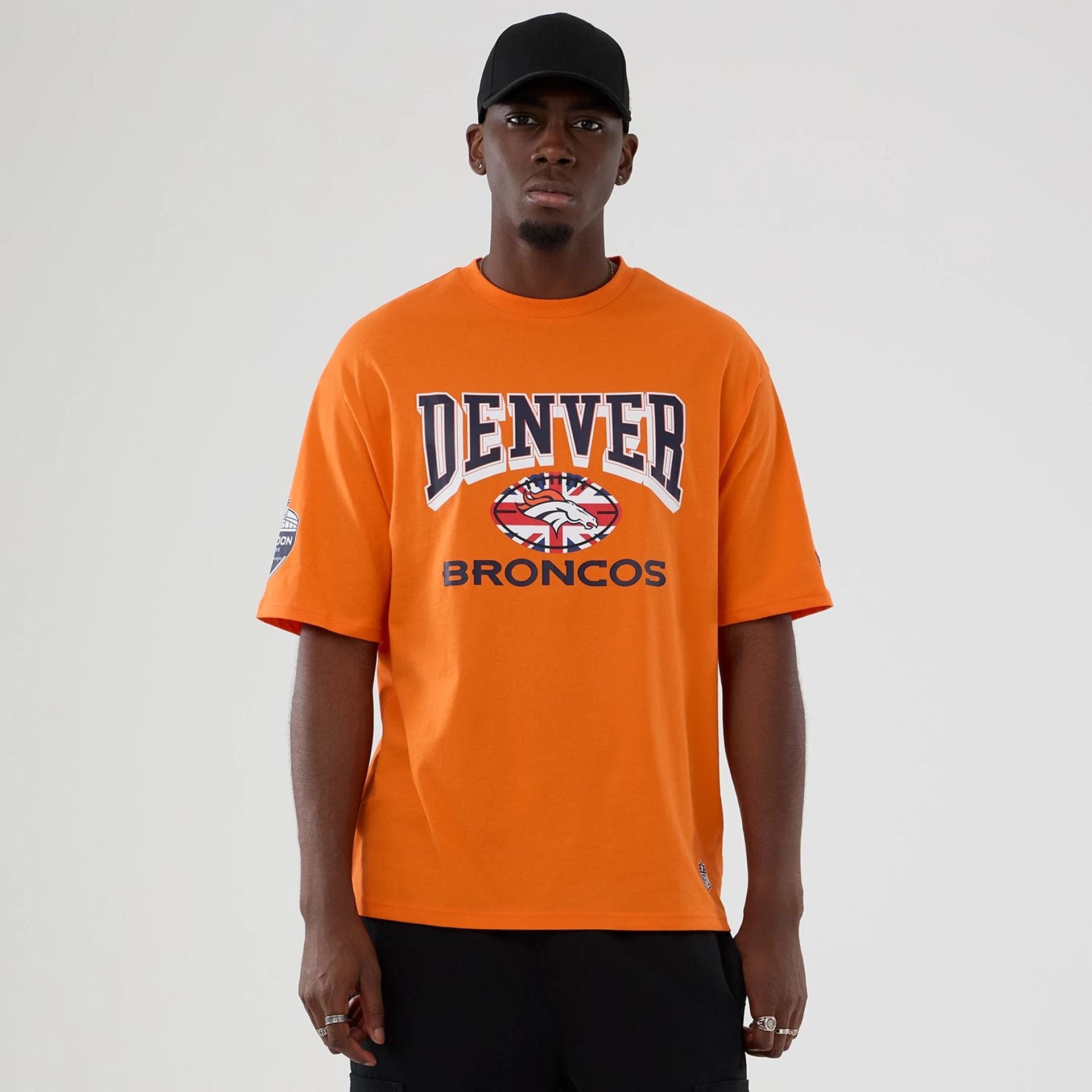 The Male model is wearing Denver Broncos NFL International Series Games 2025 Orange Oversized T-Shirt  1