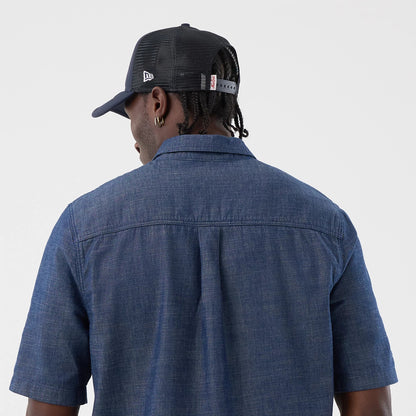 New Era Denim Blue Short Sleeve Shirt, back view on a model wearing a cap, showing the shirt’s classic collar and short sleeves with a straight back yoke, alongside contrast stitching on a textured denim fabric.