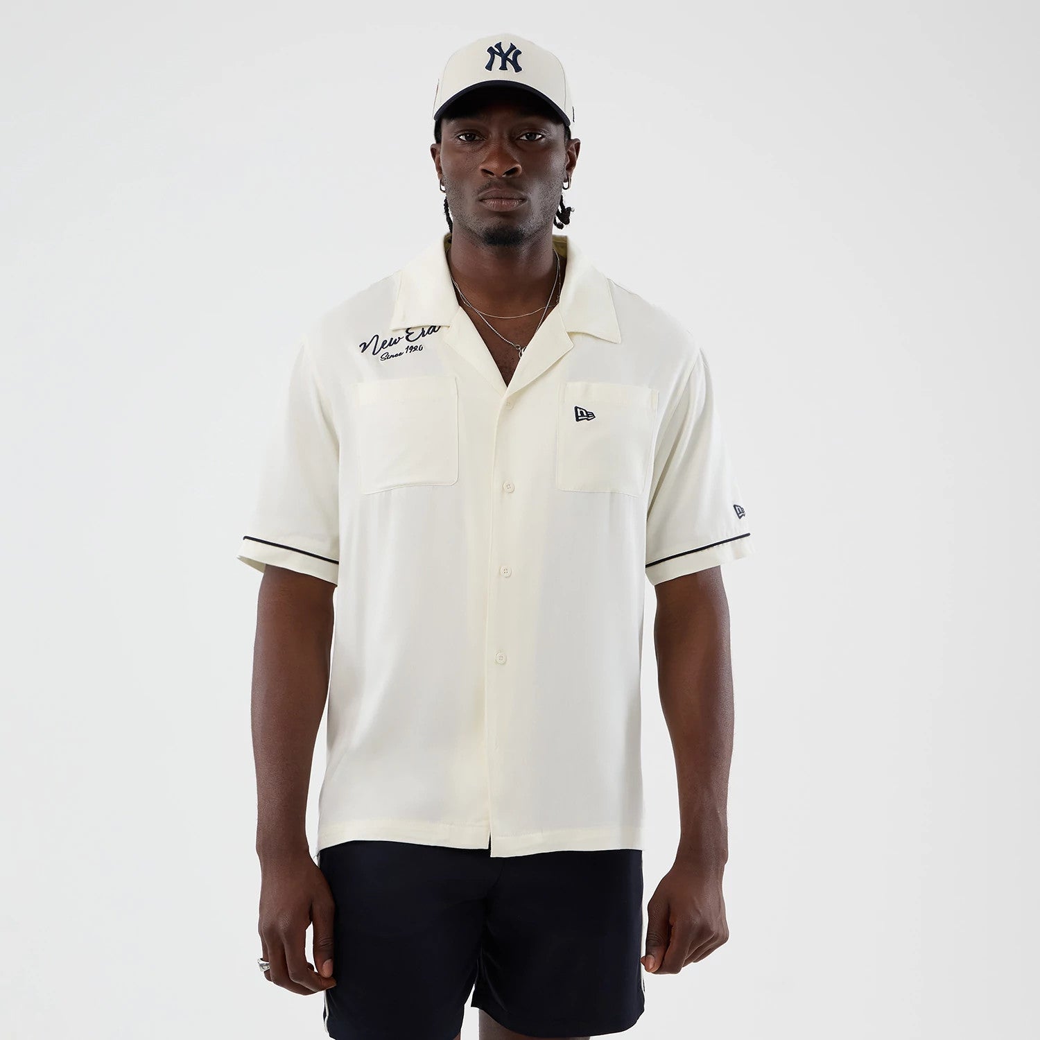 The model is wearing this New Era Graphic Revere Short Sleeve Shirt in open white. 1