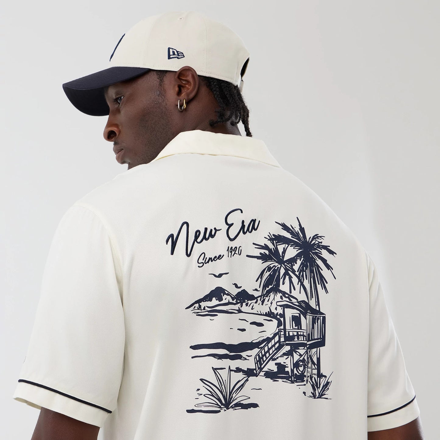The model is wearing this New Era Graphic Revere Short Sleeve Shirt in open white. 4
