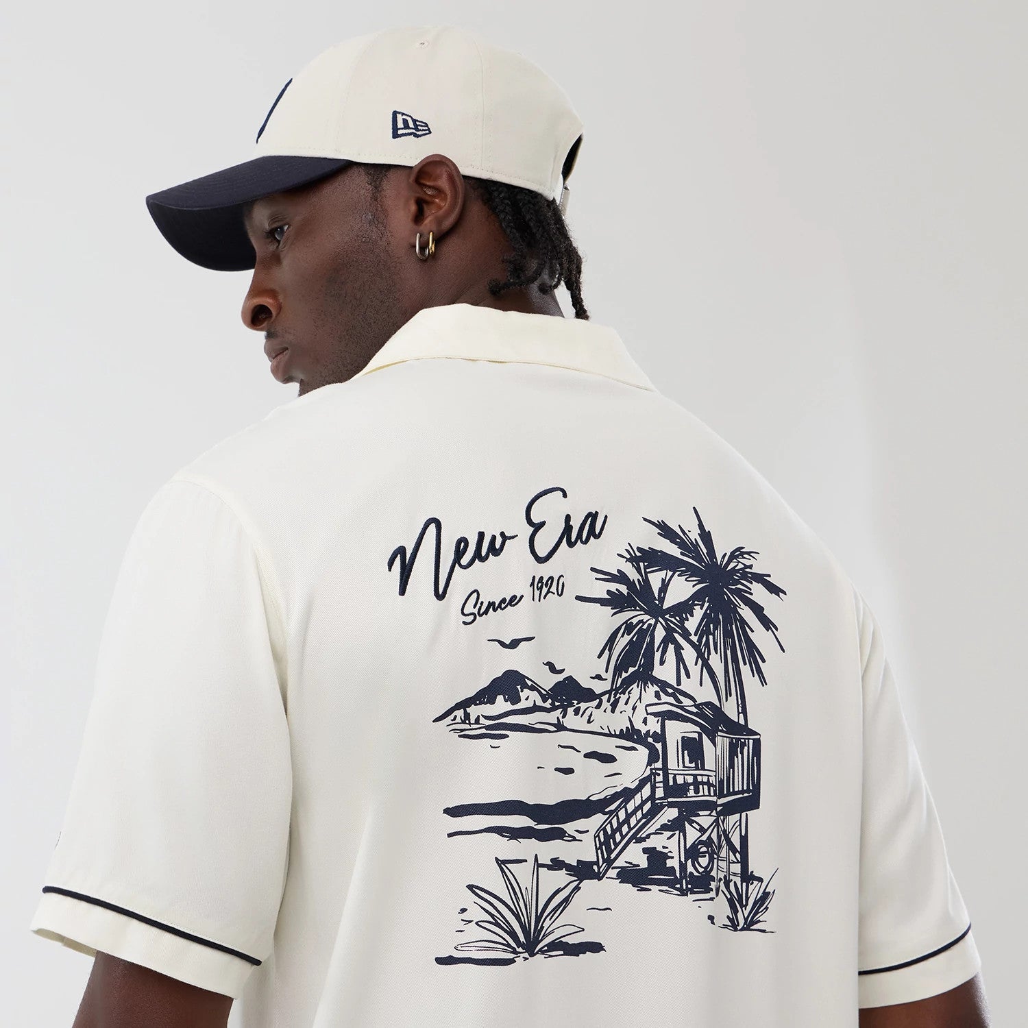 The model is wearing this New Era Graphic Revere Short Sleeve Shirt in open white. 4