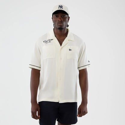 The model is wearing this New Era Graphic Revere Short Sleeve Shirt in open white. 1