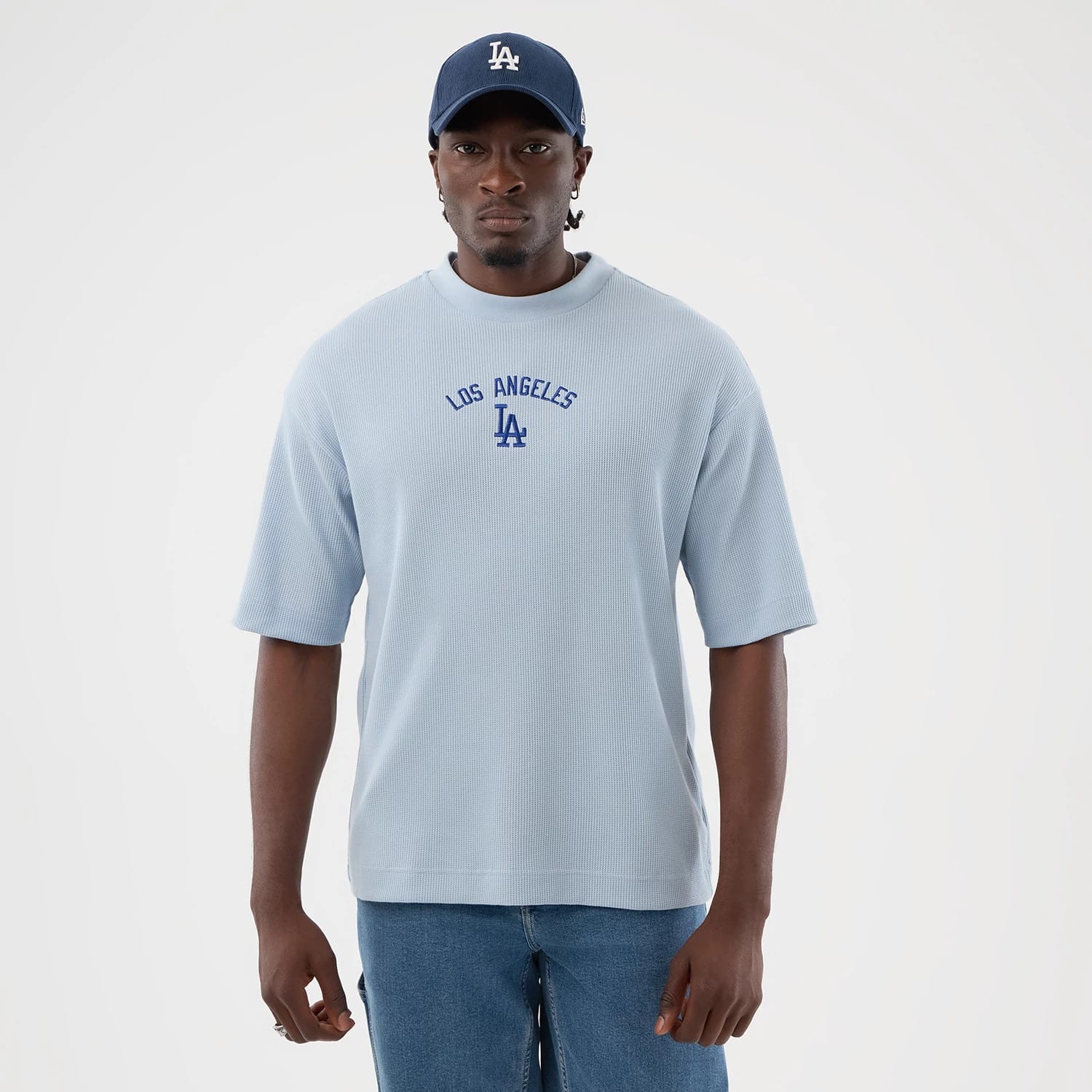 New Era LA Dodgers MLB Waffle Pastel Blue T-Shirt, front view on-model showing the short-sleeved pastel blue top with an embroidered Los Angeles and LA logo in blue centred on the chest, paired with denim jeans and a blue cap for a coordinated look.