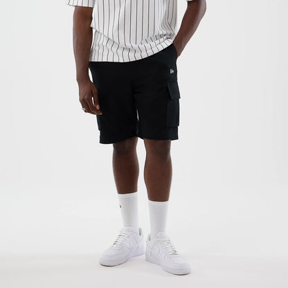 New Era Black Cargo Shorts, front view featuring double cargo pockets on each side, a small embroidered New Era logo near the waistband, styled on-model with a white pinstripe t-shirt and white trainers.