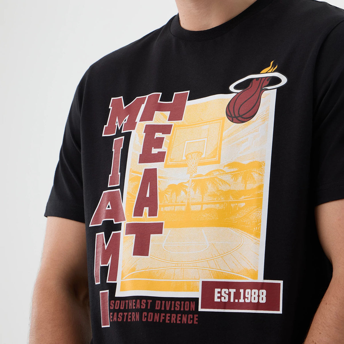 New Era Miami Heat NBA Graphic Black T-Shirt, front view showing a large yellow and maroon basketball court graphic with Miami Heat lettering running vertically, the team logo prominently printed at the top right, and EST. 1988 in on the bottom left.
