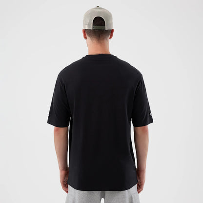 New Era New York Mets MLB Icon Graphic Black T-Shirt, back view on-model showcasing a plain black design with short sleeves, the New Era logo embroidered on the left sleeve, and the model styled with a beige cap and grey shorts.