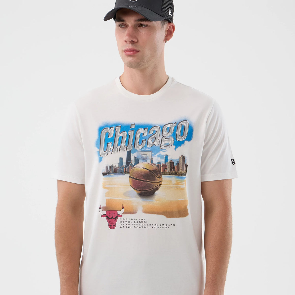 New Era Chicago Bulls NBA Beach Graphic White T-Shirt, front view on-model featuring a large basketball and cityscape graphic with 'Chicago' lettering across the chest, an embroidered New Era logo on the sleeve, and a Bulls logo at the bottom left.