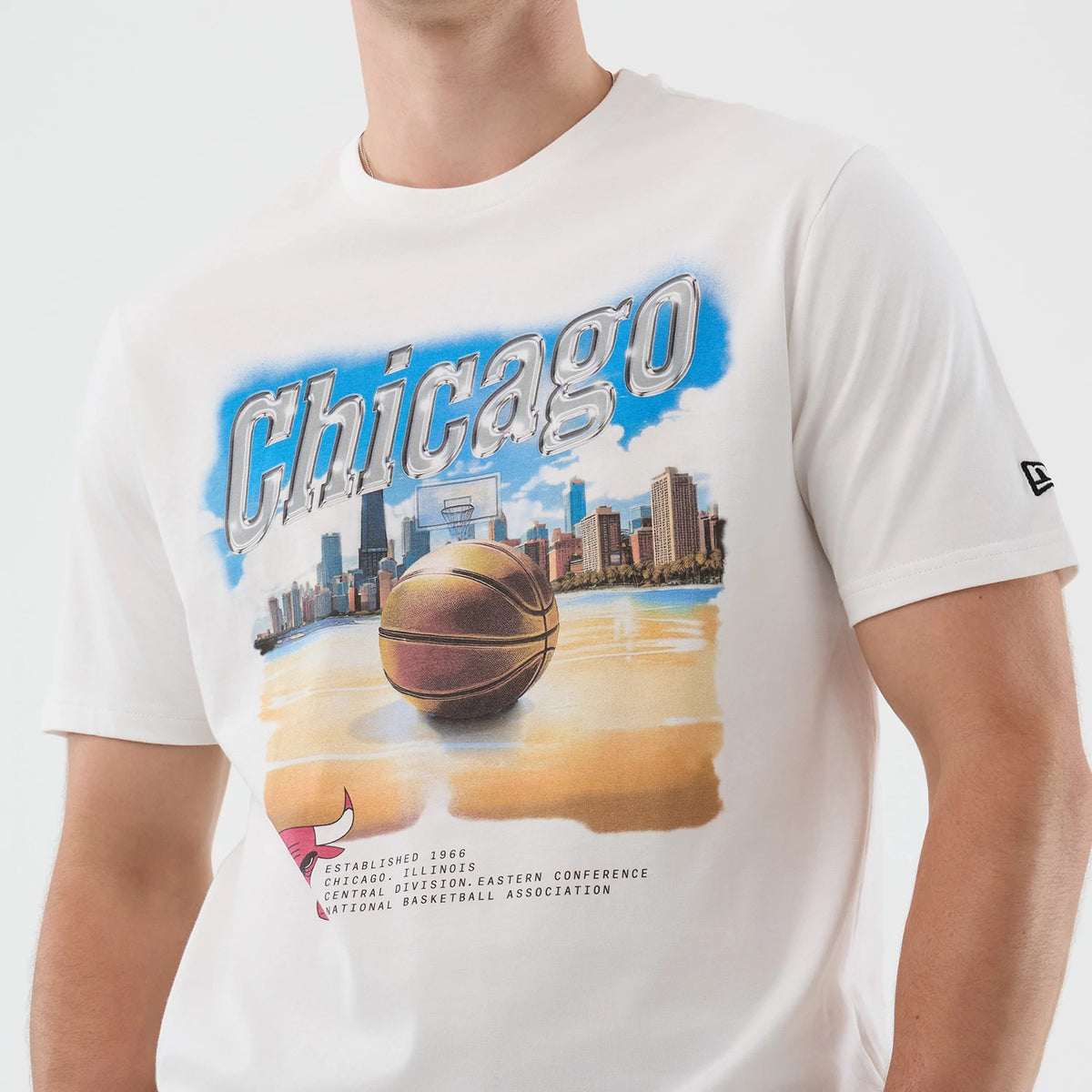 New Era Chicago Bulls NBA Beach Graphic White T-Shirt, front view showing a large colourful graphic with a basketball, skyline, and Chicago lettering, the Bulls logo near the bottom and an embroidered New Era logo on the left sleeve.