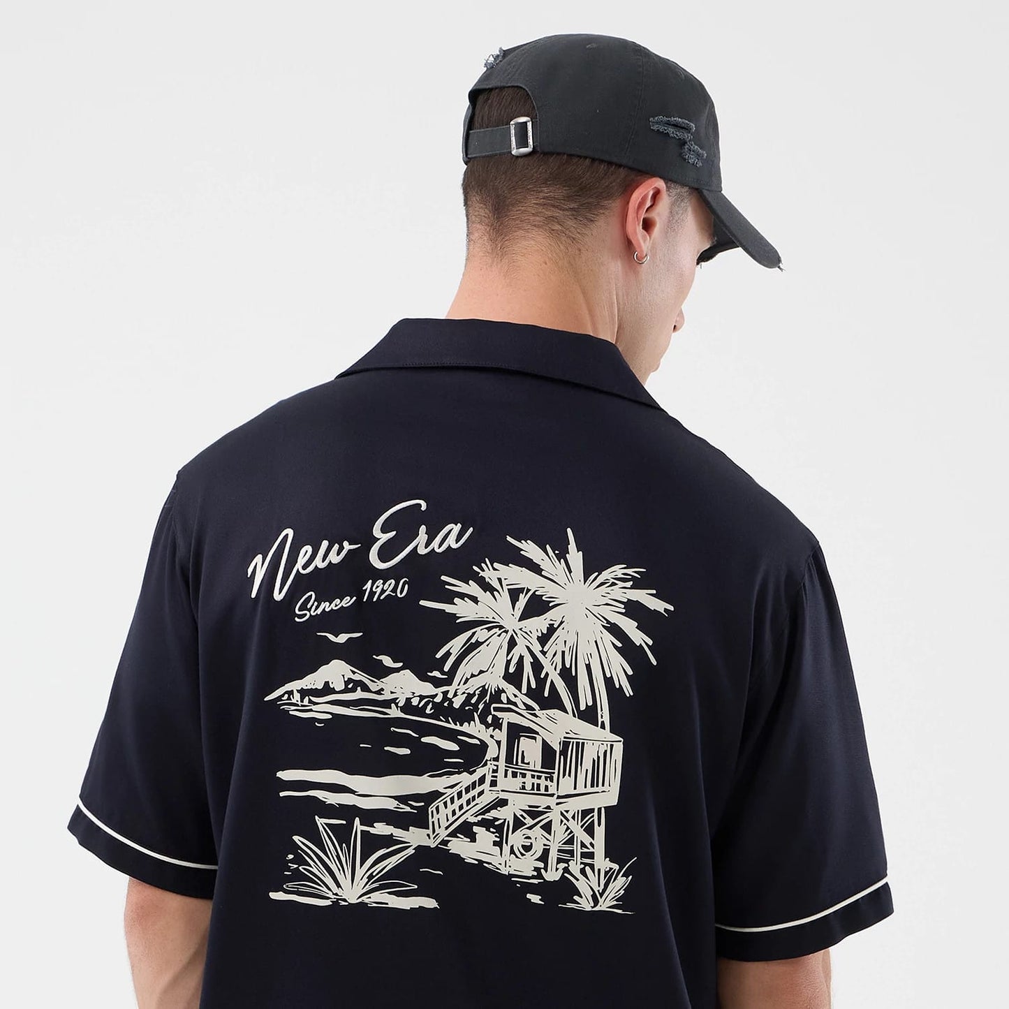 The model is wearing this New Era Graphic Revere Short Sleeve Shirt in navy. 5