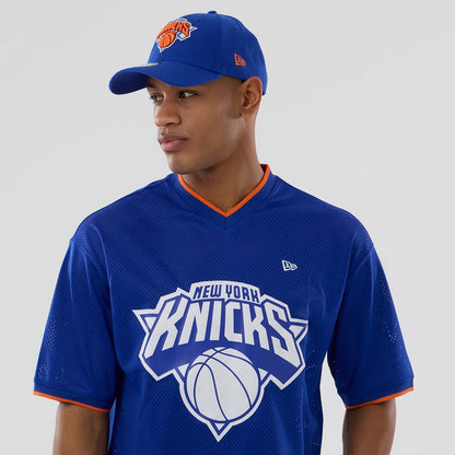 New Era New York Knicks NBA Mesh Blue Oversized T-Shirt, front view on-model showing the large white team logo with basketball graphic across the chest, small embroidered New Era logo on the left chest, and orange trim on the neckline and cuffs.