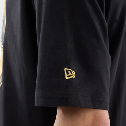 New Era Sticker Lisbon Black Oversized T-Shirt, on-model view focusing on the short sleeve, featuring a prominent yellow embroidered New Era logo near the hem and a glimpse of a light graphic on the body of the shirt.