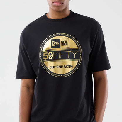 New Era Sticker Copenhagen Black Oversized T-Shirt, front view featuring a large gold-printed circular sticker design in the centre with New Era and 59FIFTY logos, Copenhagen text below, and short sleeves styled on a model.