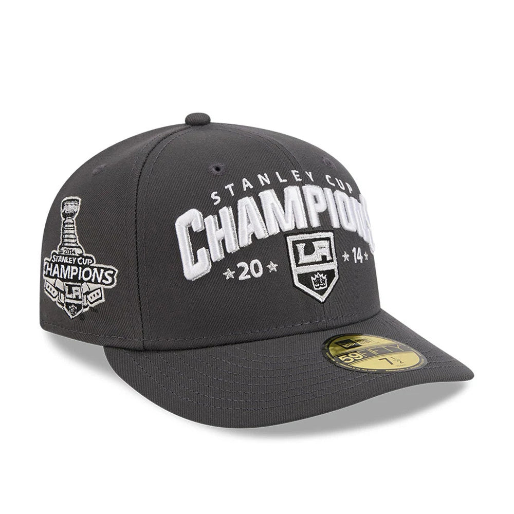 LA Kings NHL Stanley Cup Champions Dark Grey New Era 59FIFTY Fitted Cap, front view showing raised white embroidered Champions lettering and LA Kings logo on the crown, with side Stanley Cup patch and gold 59FIFTY size sticker on the visor.