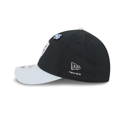 Raiders NFL Draft 2026 Black New Era 39THIRTY M-Crown Stretch Fit Cap, side view showing the silver embroidered New Era flag logo on the black structured crown, with light grey curved visor and a draft pin attached near the eyelet.