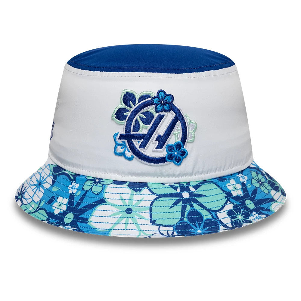 New Era TGR Haas F1 Japan Race Special White Bucket Hat, front view showing a blue and turquoise embroidered logo surrounded by floral patterns on the white crown, with a floral print in blue and green tones on the visor.
