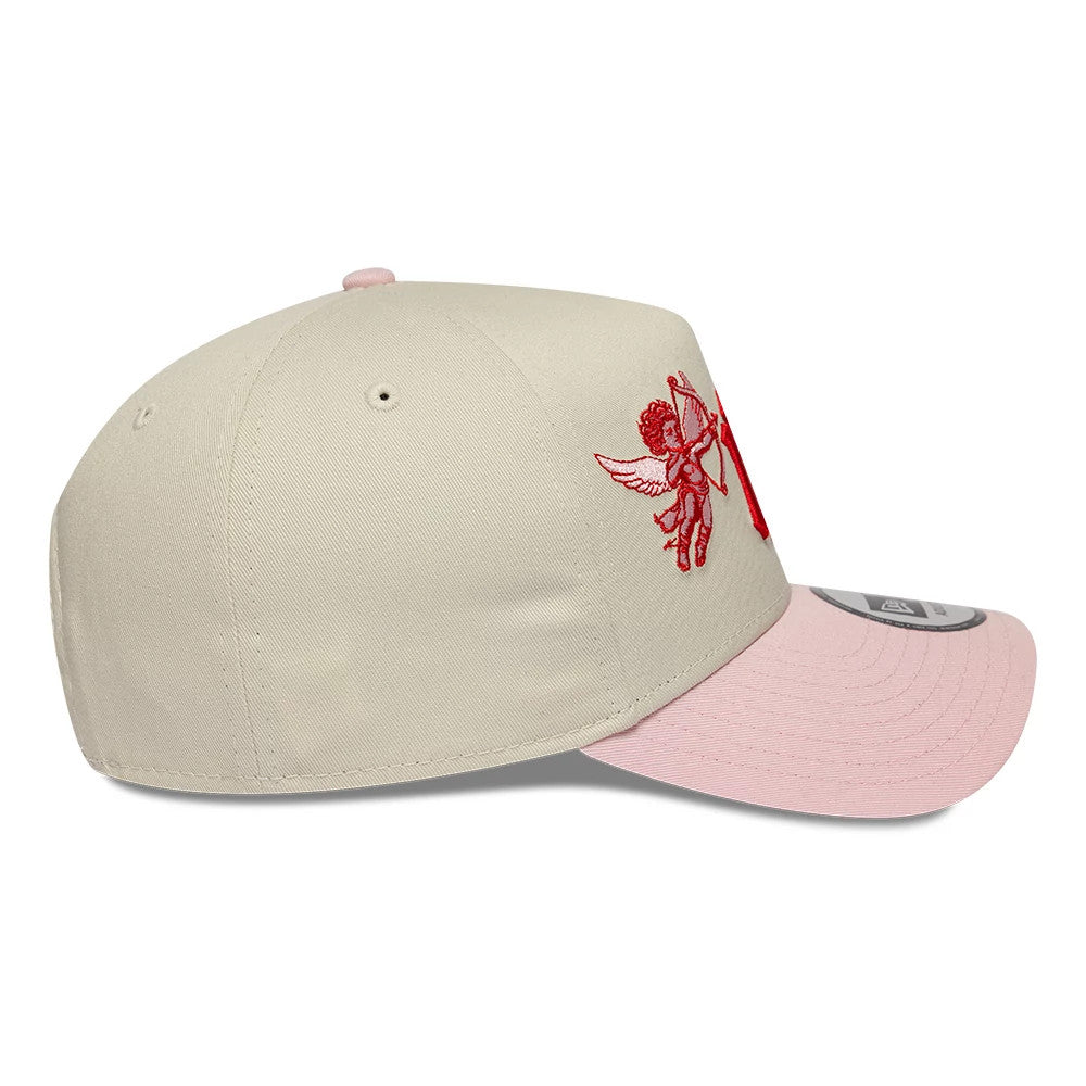 New York Yankees MLB Cherub Cream & Pink New Era 9FORTY A-Frame Adjustable Cap, side view showing a red embroidered cherub on the cream crown, a curved pink visor with 9FORTY size sticker, and a pink top button.