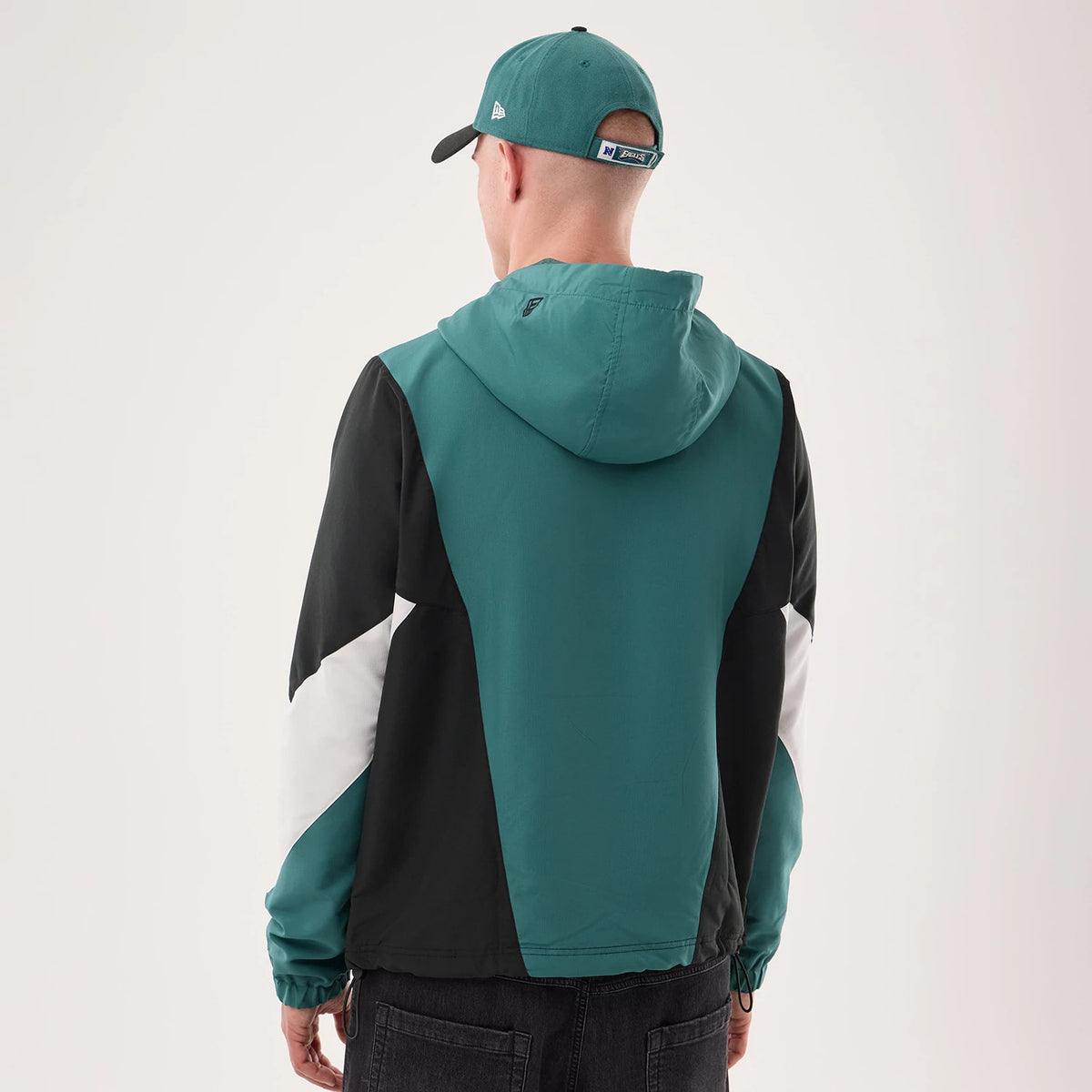 New Era Philadelphia Eagles NFL Dark Green Jacket, back view on a model with a matching cap, showing a dark green hood and back panel, contrasting black side panels and white on the sleeves, creating a dynamic and sporty colour block design.