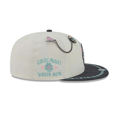 White Sox MLB Day Of The Dead Light Beige & Black New Era 59FIFTY Fitted Cap, three-quarter view showing the turquoise and pink embroidered Chicago White Sox logo on the back, with decorative pins and chain on the light beige crown.