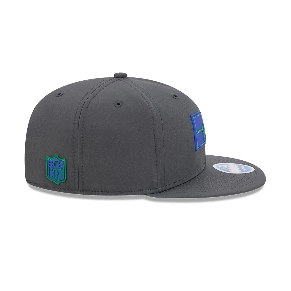 Seahawks NFL Sideline 2026 Charcoal New Era 9FIFTY Snapback Adjustable Cap, side view showing the blue and green New Era logo on the left panel, grey flat visor, and the embroidered NFL shield logo at the centre back.