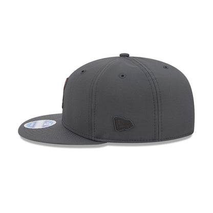 Browns NFL Sideline 2026 Charcoal New Era 9FIFTY Snapback Adjustable Cap, side view showing the black embroidered New Era flag logo on the left side panel, charcoal flat visor with a 9FIFTY size sticker, and matching top button.