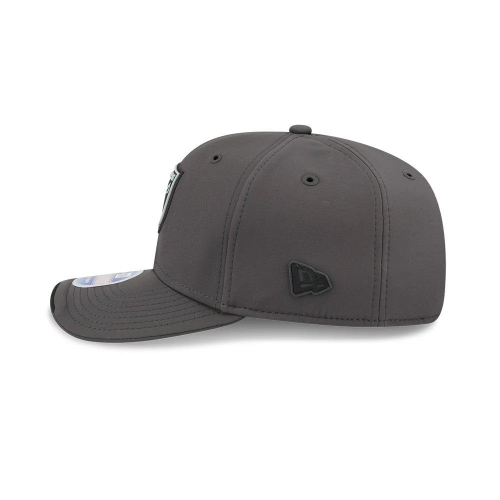 Raiders NFL Sideline 2026 Charcoal New Era 9SEVENTY Stretch Snap Adjustable Cap, side view showing the black embroidered New Era flag logo on the left side panel, a structured charcoal crown, and a curved visor with a 9SEVENTY size sticker.