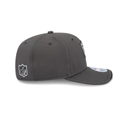 Raiders NFL Sideline 2026 Charcoal New Era 9SEVENTY Stretch Snap Adjustable Cap, side view showing the black and white NFL shield logo on the left side, the charcoal structured crown with black eyelets.