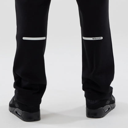 New Era Tech Reflective Black Straight Leg Joggers, rear view showing reflective strips across the lower legs and a New Era logo near the right strip, with a relaxed fit over black trainers.