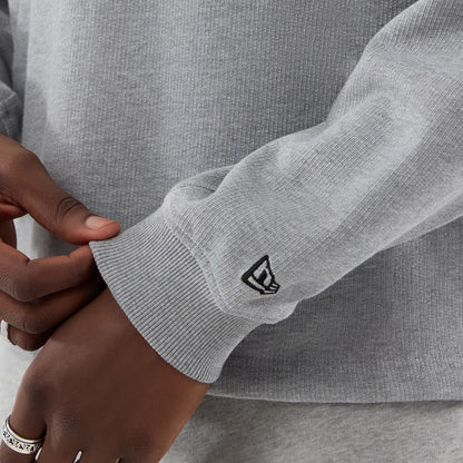 New Era Grey Oversized Crew Neck Sweater, close-up view showing a ribbed cuff with a small black embroidered New Era flag logo, grey fabric texture with knit pattern, and the sweater’s relaxed fit design.