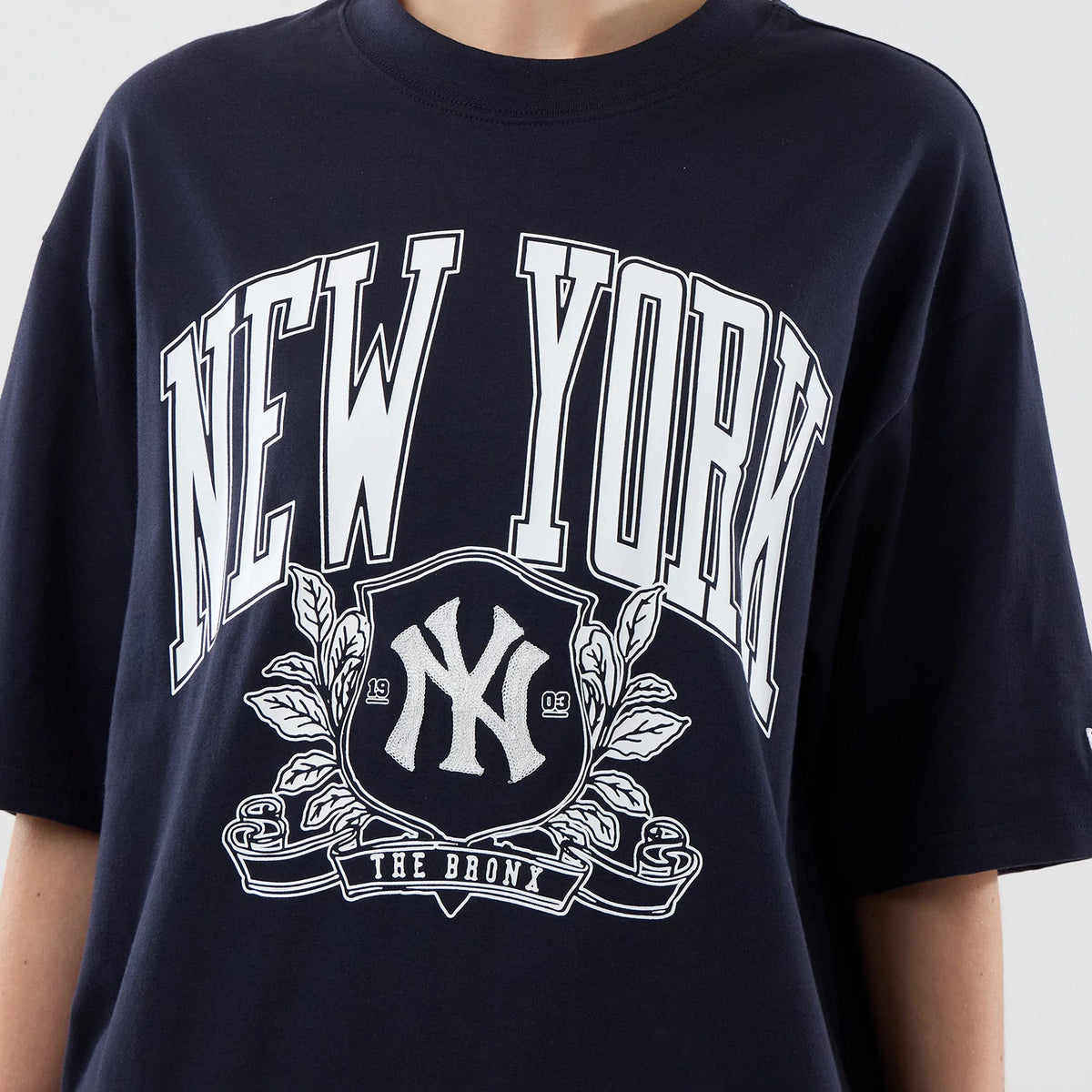 New Era New York Yankees MLB Arch Graphic Navy Oversized T-Shirt, front view highlighting the white embroidered New York lettering across the chest, a central Yankees logo framed by detailed decorative leaf patterns and a The Bronx ribbon below.