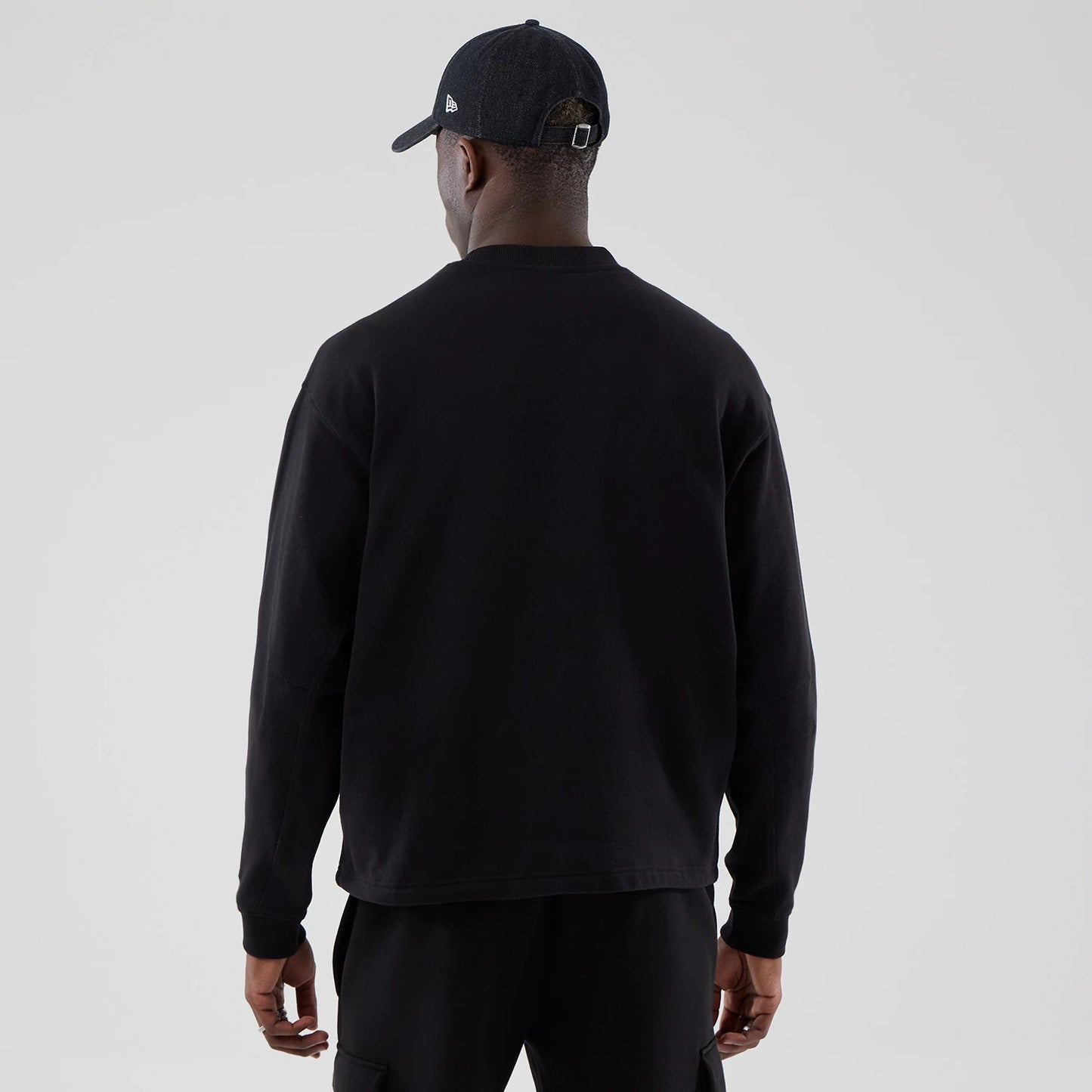 The model is wearing this New Era Oversized Crew Neck Sweater in black. 2