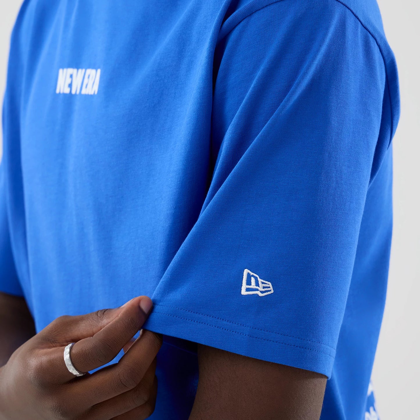 The model is wearing this New Era Cap Graphic Oversized T-Shirt in bright blue. 7