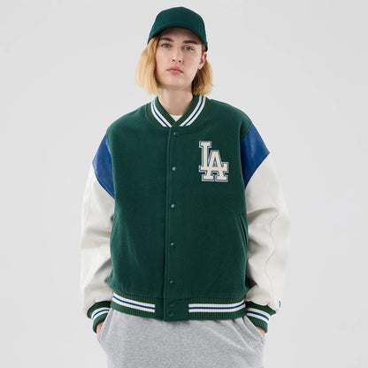 New Era LA Dodgers MLB Varsity Dark Green Jacket, front view on a model featuring a large embroidered LA logo on the left chest, contrasted white sleeves with blue accents, and ribbed green and white striped cuffs and collar.