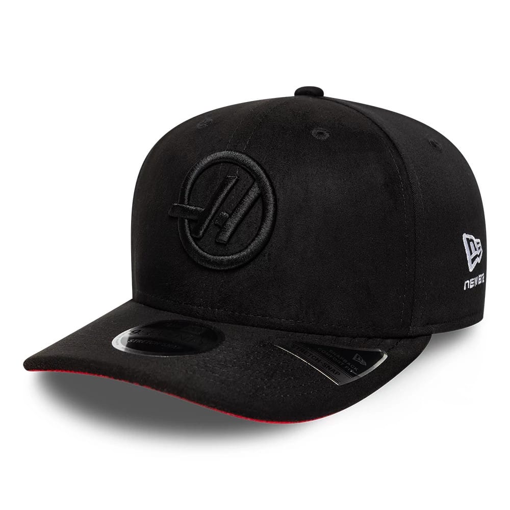 TGR Haas F1 Team Suede Black New Era 9SEVENTY Stretch Snap Adjustable Cap, three-quarter view showing the black suede fabric with an embroidered TGR logo on the front panel, a New Era flag logo on the left side, and a contrasting red undervisor edge.