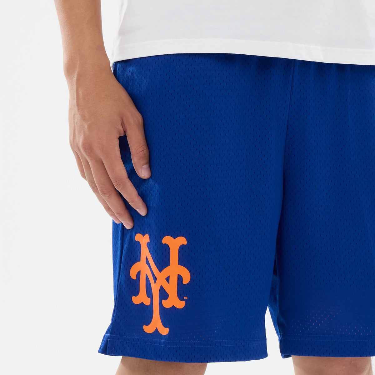 New Era New York Mets MLB Evergreen Blue Shorts, front view on a model with a white top, featuring an orange printed New York Mets logo on the lower left leg of the blue shorts, with perforations across the fabric.