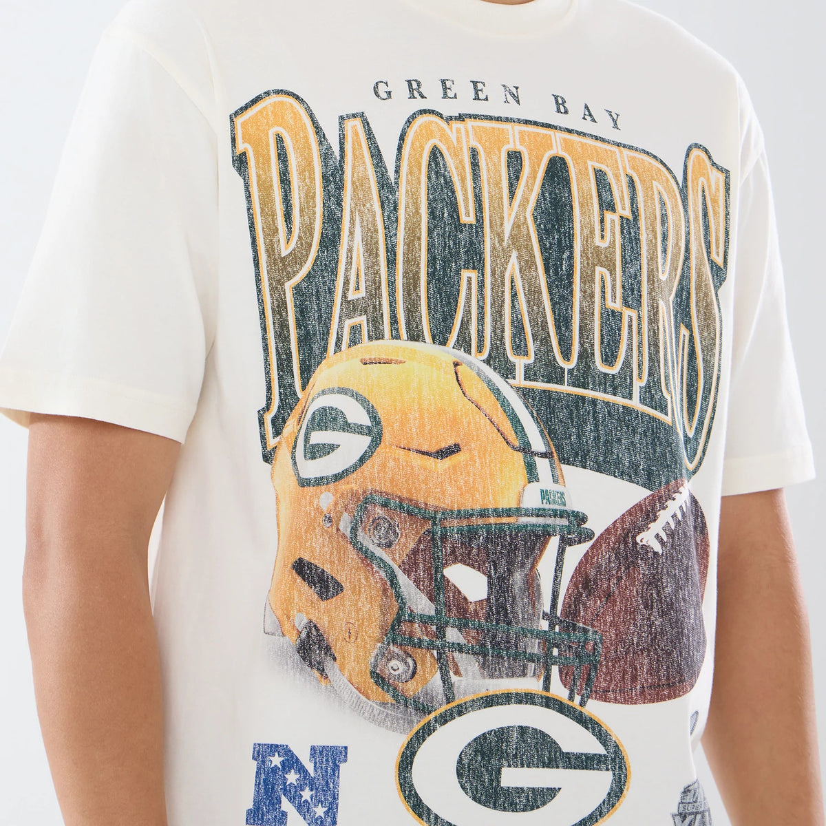 New Era Green Bay Packers NFL Sport Classic Cream T-Shirt, front view showing a large graphic of a yellow helmet and an American football, with Packers lettering across the chest, and printed Green Bay text above the design.