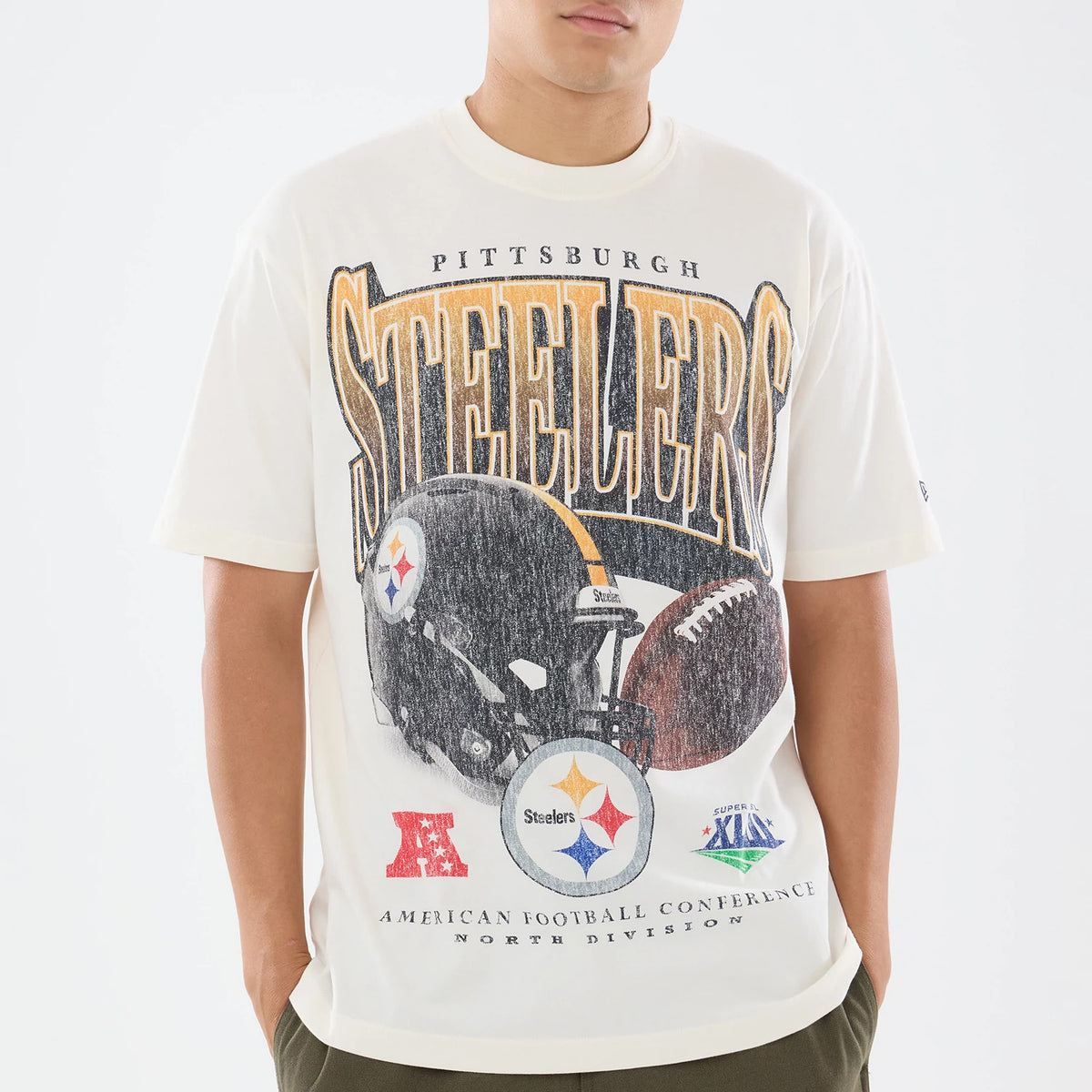 New Era Pittsburgh Steelers NFL Sport Classic Cream T-Shirt, front view on a model showing a large Pittsburgh Steelers graphic with a football helmet and ball, STEELERS lettering above, and team and conference logos printed along the lower section.