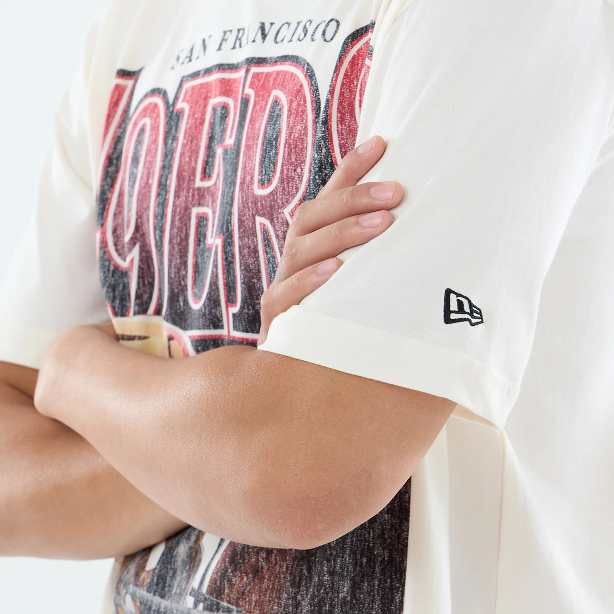New Era San Francisco 49ers NFL Sport Classic Cream T-Shirt, front view on-model showing the large red and black 49ers graphic across the chest, the New Era embroidered logo on the left sleeve, and the cream fabric detail adding to the retro design.