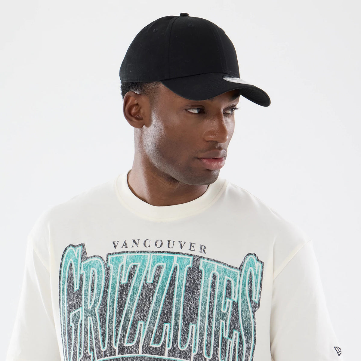 New Era Vancouver Grizzlies NBA Sport Classic Cream T-Shirt, front view on a model paired with a black cap, featuring Grizzlies text in teal and black across the chest and a small embroidered New Era logo on the left sleeve.