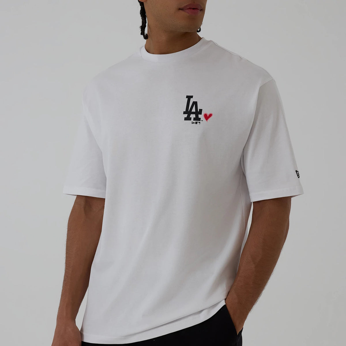 New Era LA Dodgers MLB Heart Graphic White T-Shirt, front view on a model showing a black embroidered LA Dodgers logo with a red heart on the left chest, a relaxed fit with short sleeves, and a small New Era logo on the left sleeve.