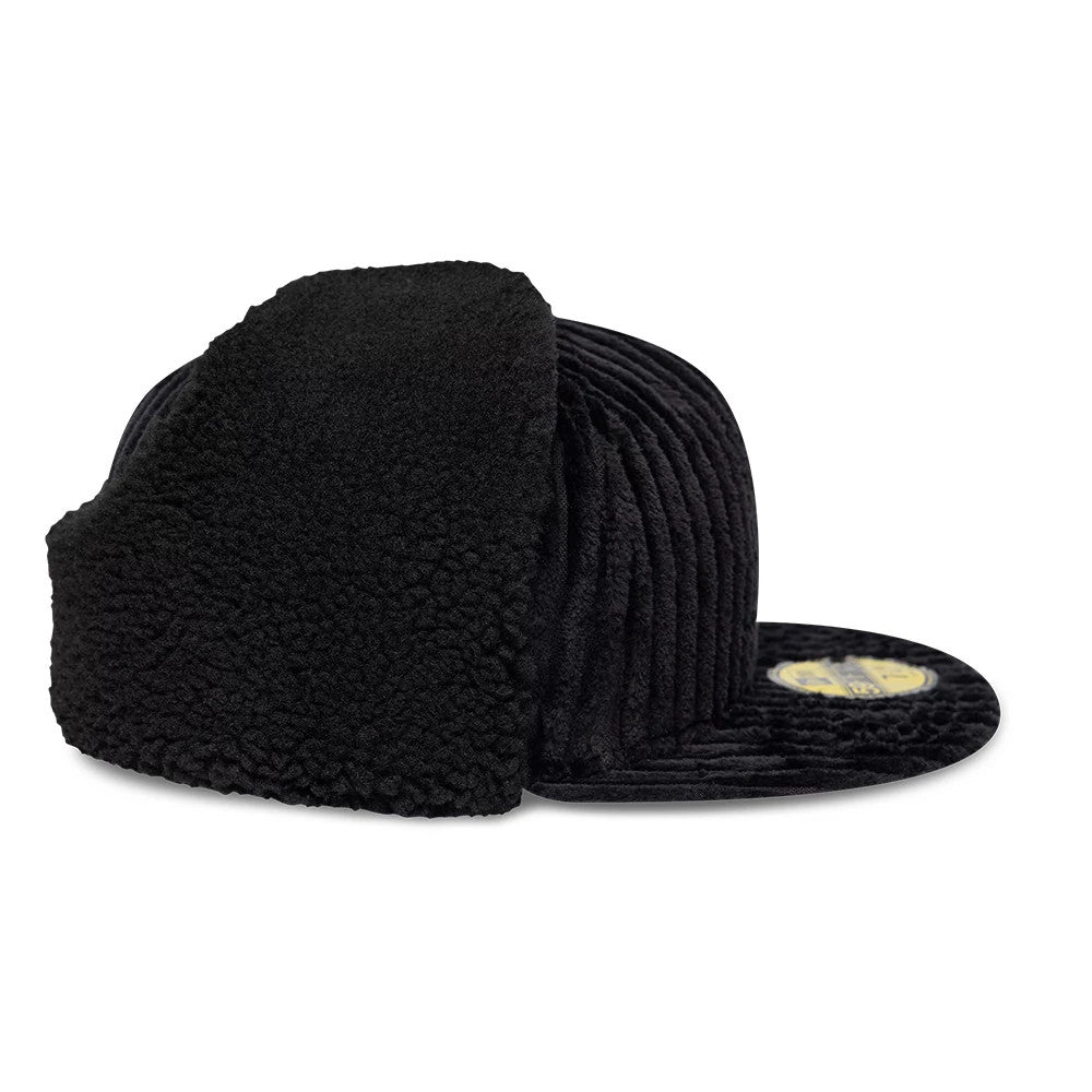 Mains X New Era Cord Black Dogear 59FIFTY Fitted Cap, side view showing the textured black corduroy fabric, prominent dogear flaps covering the sides, and a flat, black visor with a gold 59FIFTY size sticker on top.