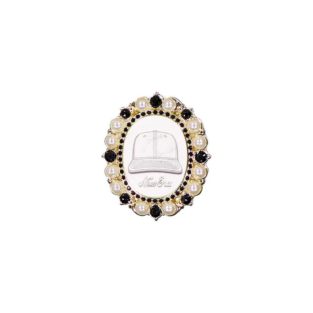 New Era 59FIFTY Day Brooch Black Pin Badge, front view showing an oval design with a stylised cap illustration and embossed New Era logo in the centre, framed by alternating black stones and pearl-like beads.
