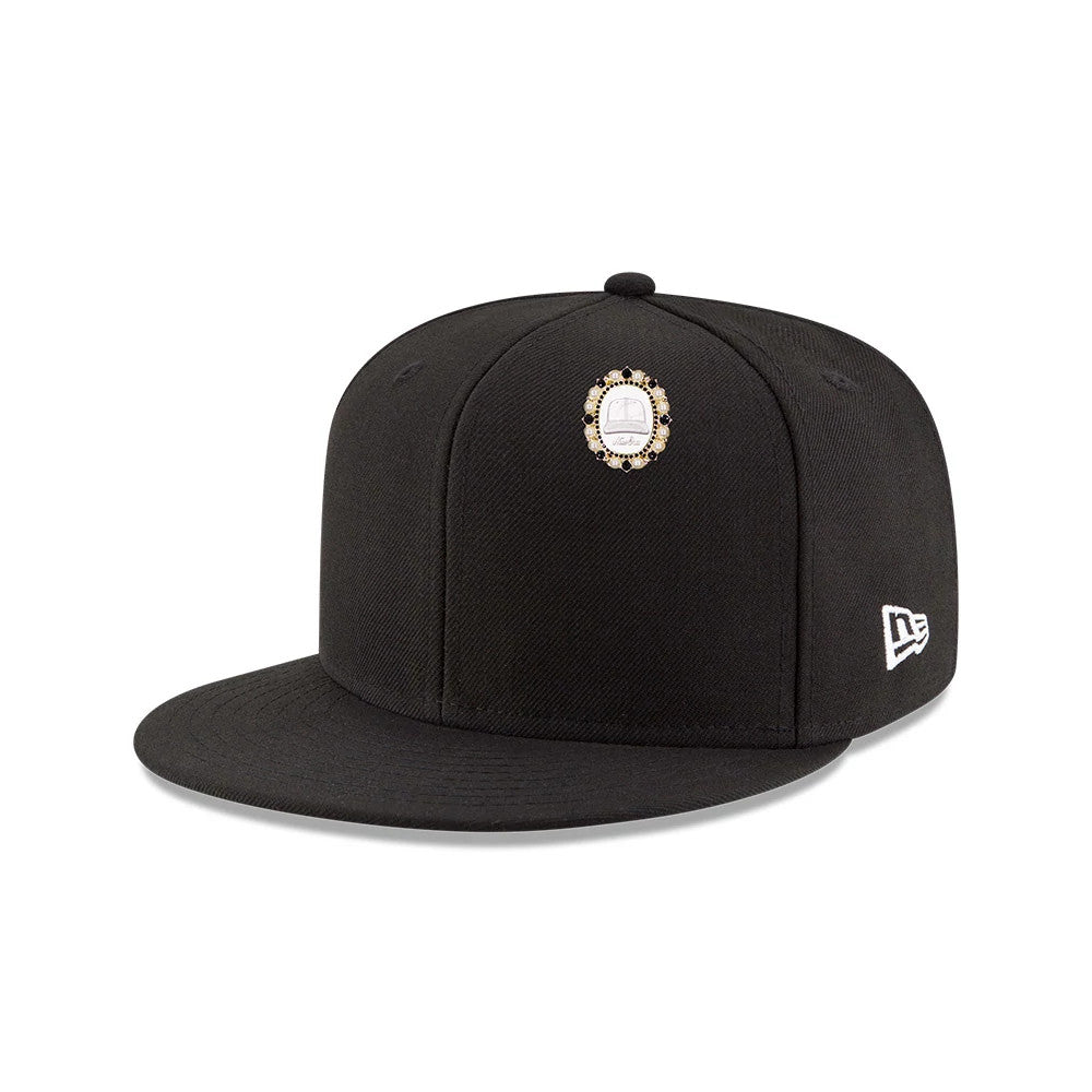 New Era 59FIFTY Day Brooch Black Pin Badge, front view showing the structured black crown with a detailed brooch pin centred on the front panel, the flat visor in matching black and an embroidered white New Era logo on the left side.