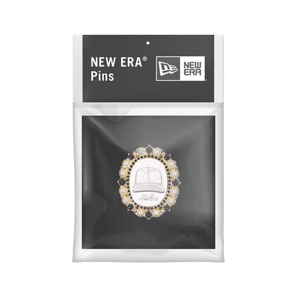 New Era 59FIFTY Day Brooch Black Pin Badge, front view in packaging showing a pin with a central cap design surrounded by sparkling gems, pearls, and a gold trim, all set against a black matte card with the New Era logo printed above.